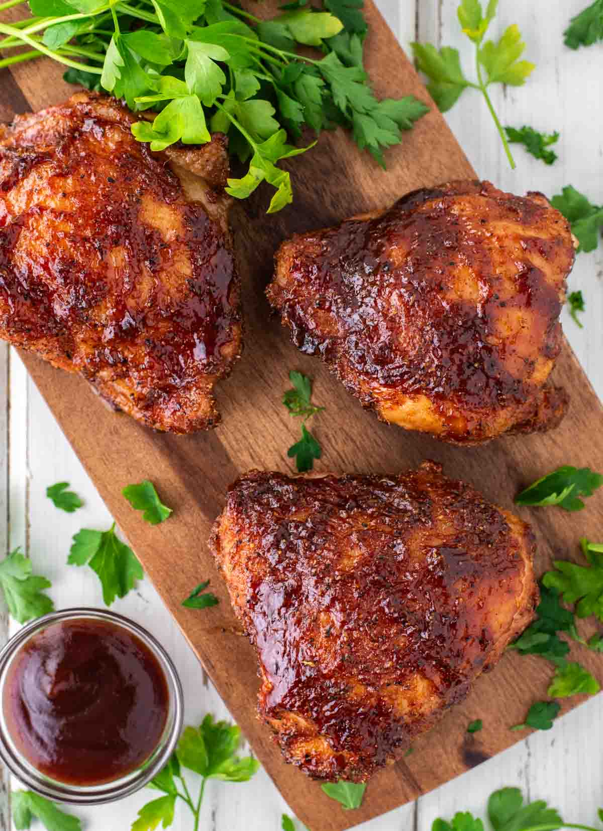 overhead shot of smoked chicken thighs on wood board with BBQ sauce