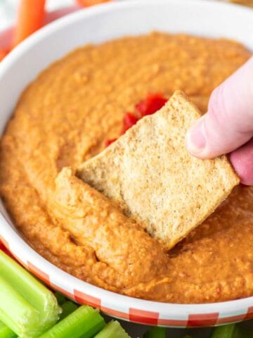pita chip being dipped in bowl of roasted red pepper hummus